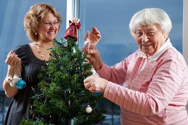 An image of an elderly person and a care worker decorating a Christmas tree
