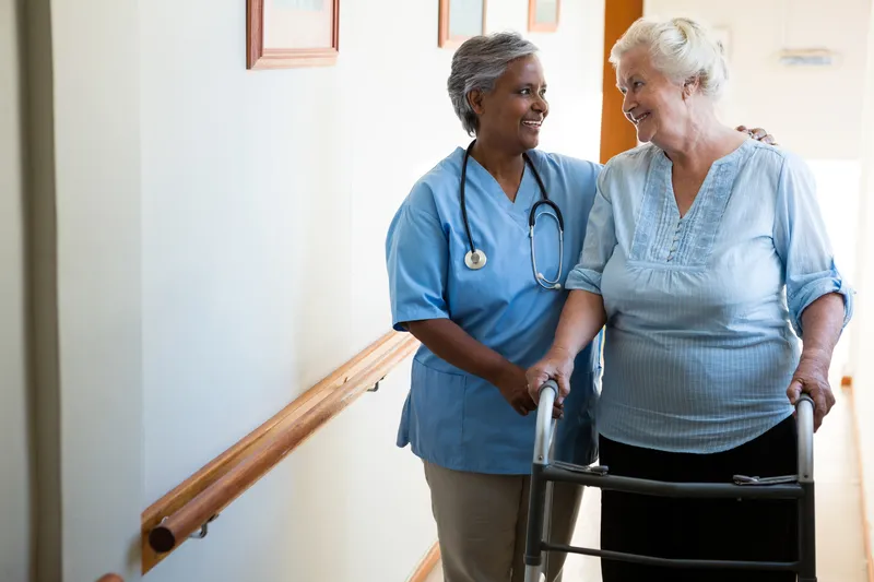 An image of a care worker helping an elderly person walk